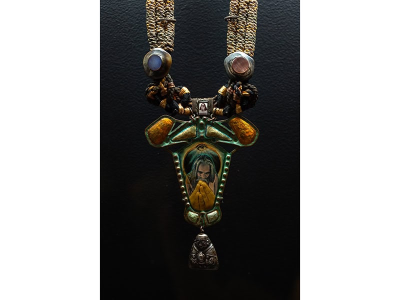 Alex and Lee (United States, est. 1970), Alex Maté (United States, 1950–1992), Lee Brooks (United States, 1940–2016), Guru Necklace, c. 197, brass, silver and gold leaf, photo collage, found object, cording, vintage horn and mother-of-pearl buttons, copper wire, 15 x 4 1/2 x 3/4 inches (381 x 114 x 19 mm), Museum of Arts and Design, New York; purchase with funds provided by the Collections Committee, 2018, shown in OUT of the Jewelry Box, Museum of Arts and Design, New York (April 20, 2024–April 12, 2026), photo: Jenna Bascom, courtesy of the Museum of Arts and Design