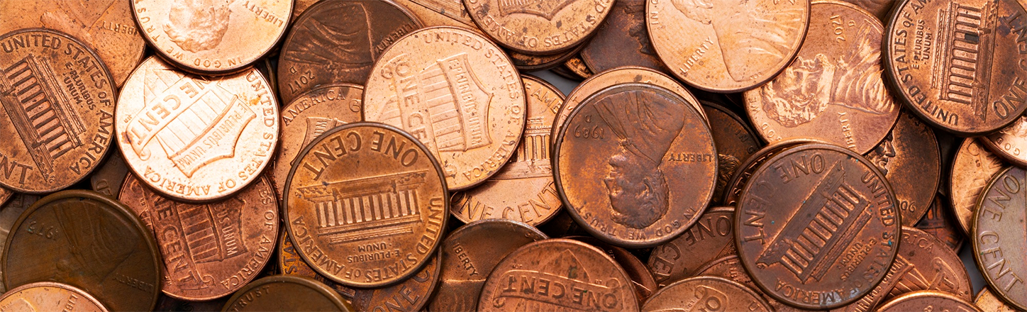 Close-up of a large pile of U.S. one-cent coins, featuring copper-plated exteriors with engravings of Lincoln's portrait and the Lincoln Memorial.