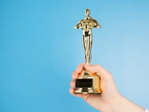 An arm holding a gold-plated Academy Award statuette on a blue background