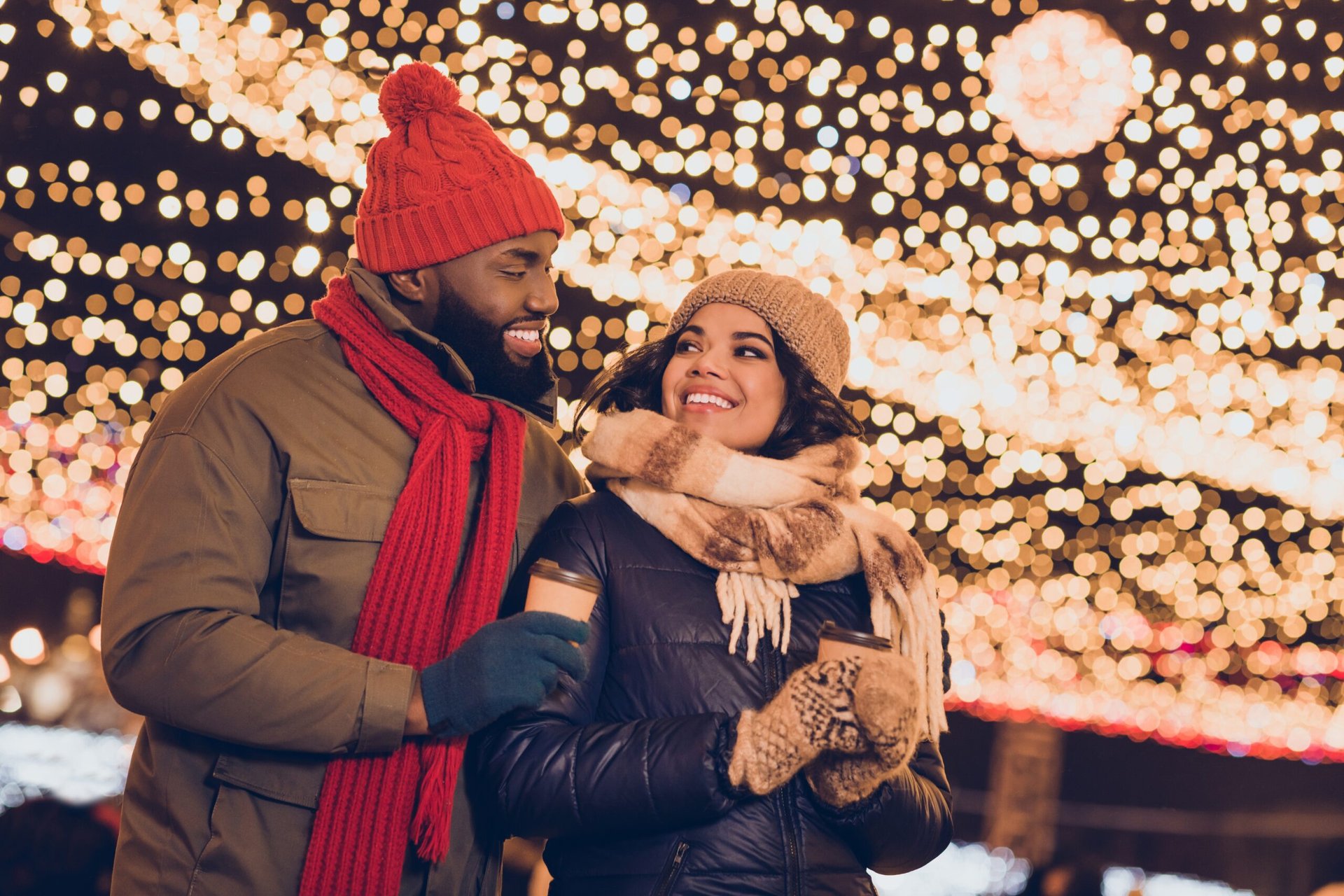 A couple walks under holiday lights, dressed in warm winter clothing.